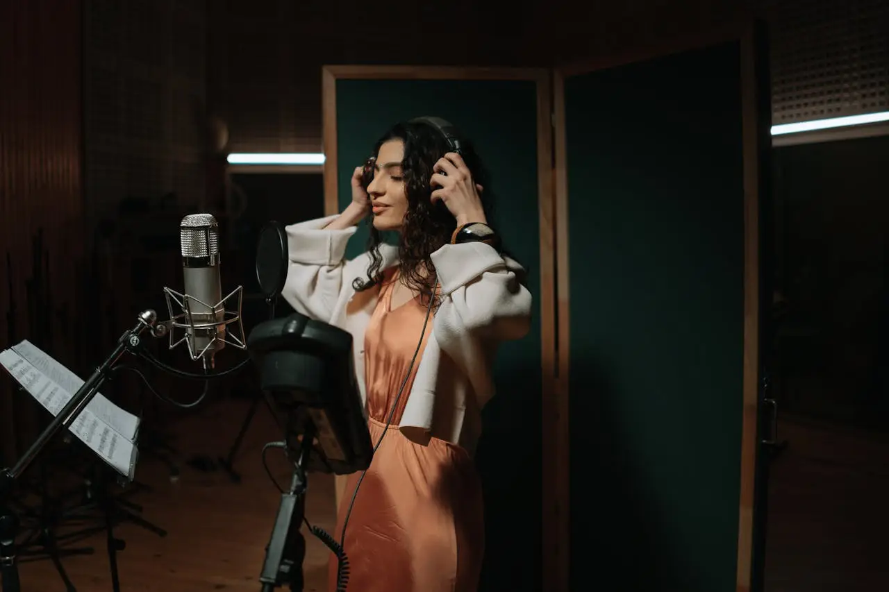 Female singer recording music in a professional studio wearing headphones and using a microphone.